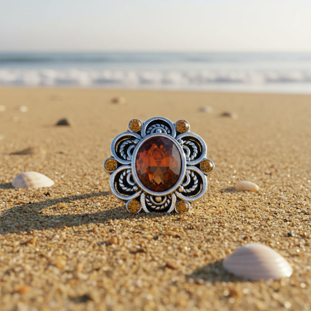 A silver-toned ornate snap button with a large faceted amber-orange oval center stone and six smaller round amber-orange accent stones