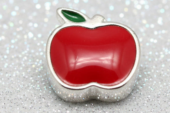 A red apple-shaped charm with a silver metal border and a small green leaf on top, shown on a black reflective background.