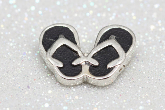 A pair of small silver flip-flop style charms or beads arranged on a glossy black reflective surface.