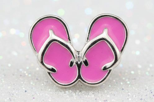 A pair of pink flip-flop sandals charm with silver metal outlines, displayed on a black reflective surface.