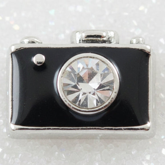 A small rectangular camera-shaped charm with a black face, silver edges, and a clear faceted rhinestone in the center, shown on a plain light background.