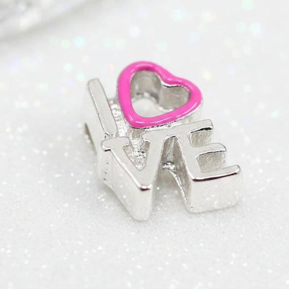 A silver-toned charm spelling 'LOVE' with a bright pink heart outline above the letter 'O', shown on a dark background.