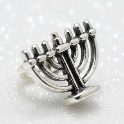 A silver-toned metal menorah charm or bead shown against a dark black background.