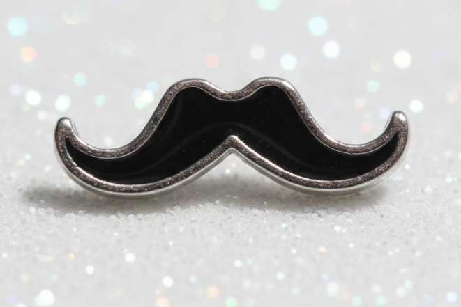 A small mustache-shaped metallic charm or bead with a polished silver border and dark center, shown on a plain light background.