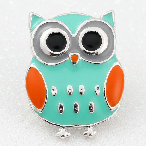 A turquoise and orange owl-shaped snap button with large silver-rimmed eyes, shown on a plain white background.