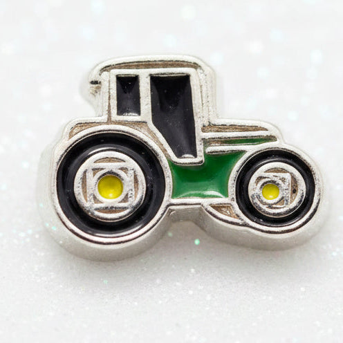 A tractor-shaped charm or bead with a silver-toned metal base and colorful enamel details, featuring black wheels, a green body, and yellow centers, set against a plain white background.