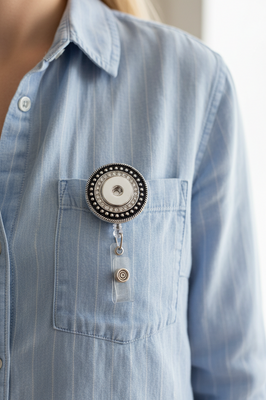 A silver-toned retractable badge reel with a circular design, featuring a black and silver beaded outer ring, a clear crystal-embellished center ring, and a clear plastic clip with a silver swivel connector.