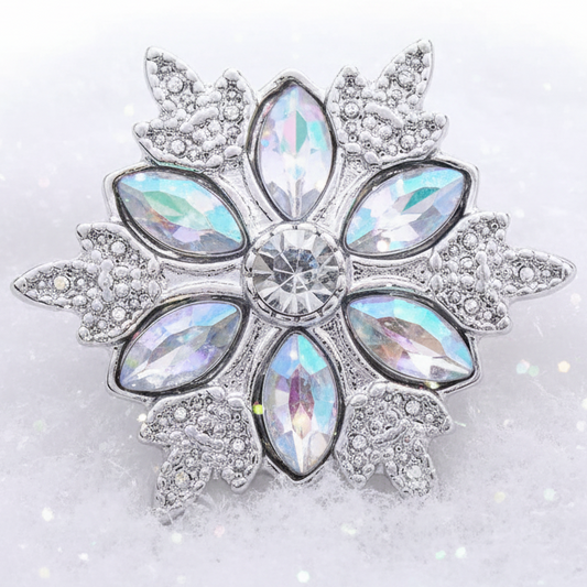 A snowflake-shaped silver statement snap featuring iridescent clear crystals in a floral pattern, set against a soft white background with subtle glitter.