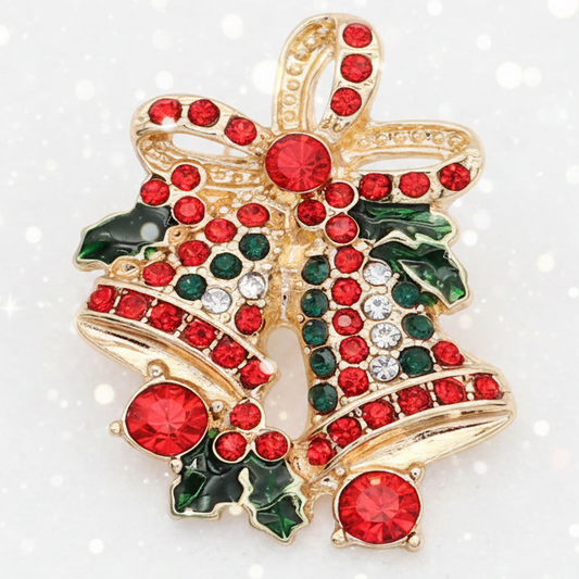 A gold-tone Christmas ornament shaped lwo hanging bells decorated with red and green rhinestones statement snap, set against a white background with subtle bokeh light effects.