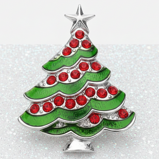 A Christmas tree-shaped snap with green enamel, silver-tone metal outlines, and red rhinestone accents, shown on a sparkly white surface against a light gray background.