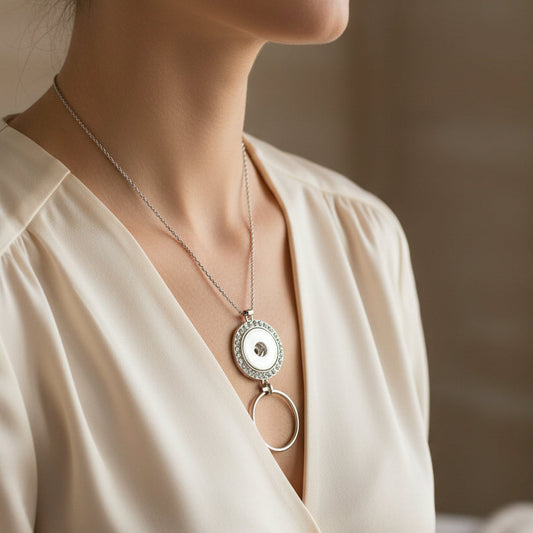 A close-up of a woman wearing a silver pendant necklace with a circular disc and dangling ring, paired with a cream satin blouse.