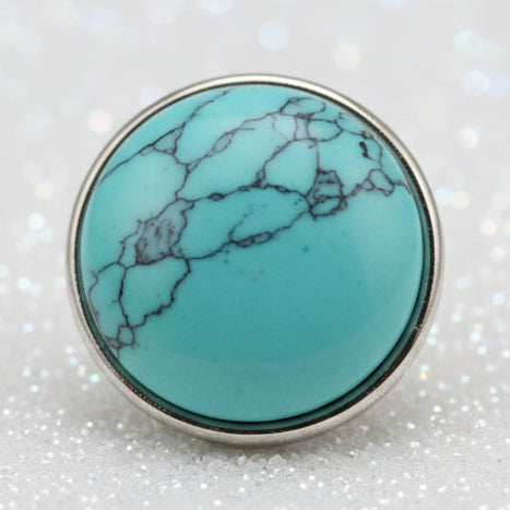 A round turquoise stone snap button with dark veining, set in a silver bezel
