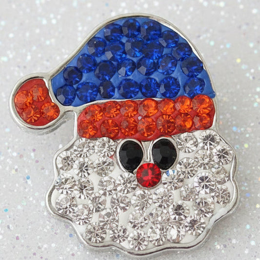 A Santa Claus face snap featuring a blue hat, red trim, black eyes, and a white beard made of clear rhinestones, set on a glittery silver background.