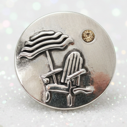 A round silver-toned snap button featuring an engraved beach chair and umbrella motif