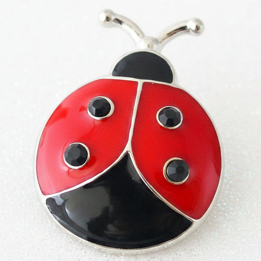 A ladybug-shaped snap button with red and black enamel wings, silver metal outlines, and small black eyes, photographed on a light textured background.