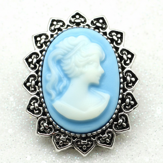 A vintage-style cameo snap button with a light blue and white profile design in a silver-toned filigree frame, displayed on a white backdrop