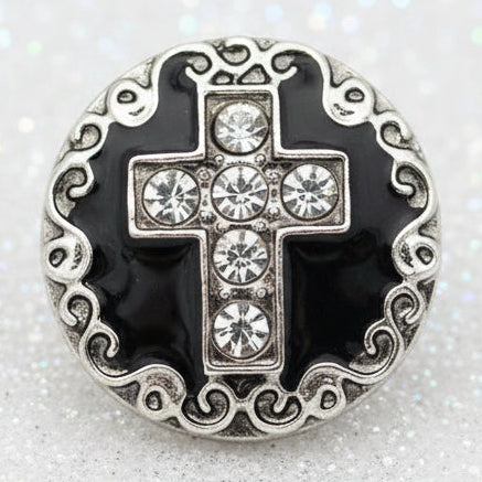 A round silver cross snap button with a black enamel background and clear rhinestones