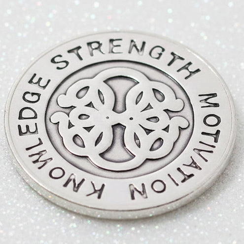 A round silver-toned metal snap button with engraved text reading 'EDGE STRENGTH MOTION KNOWLEDGE' around a central knot-like emblem