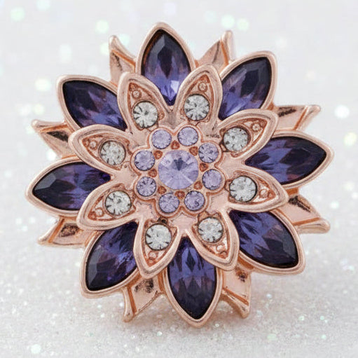 A decorative flower-shaped snap with a central purple stone surrounded by smaller clear stones, with a rose gold-colored petal outline.