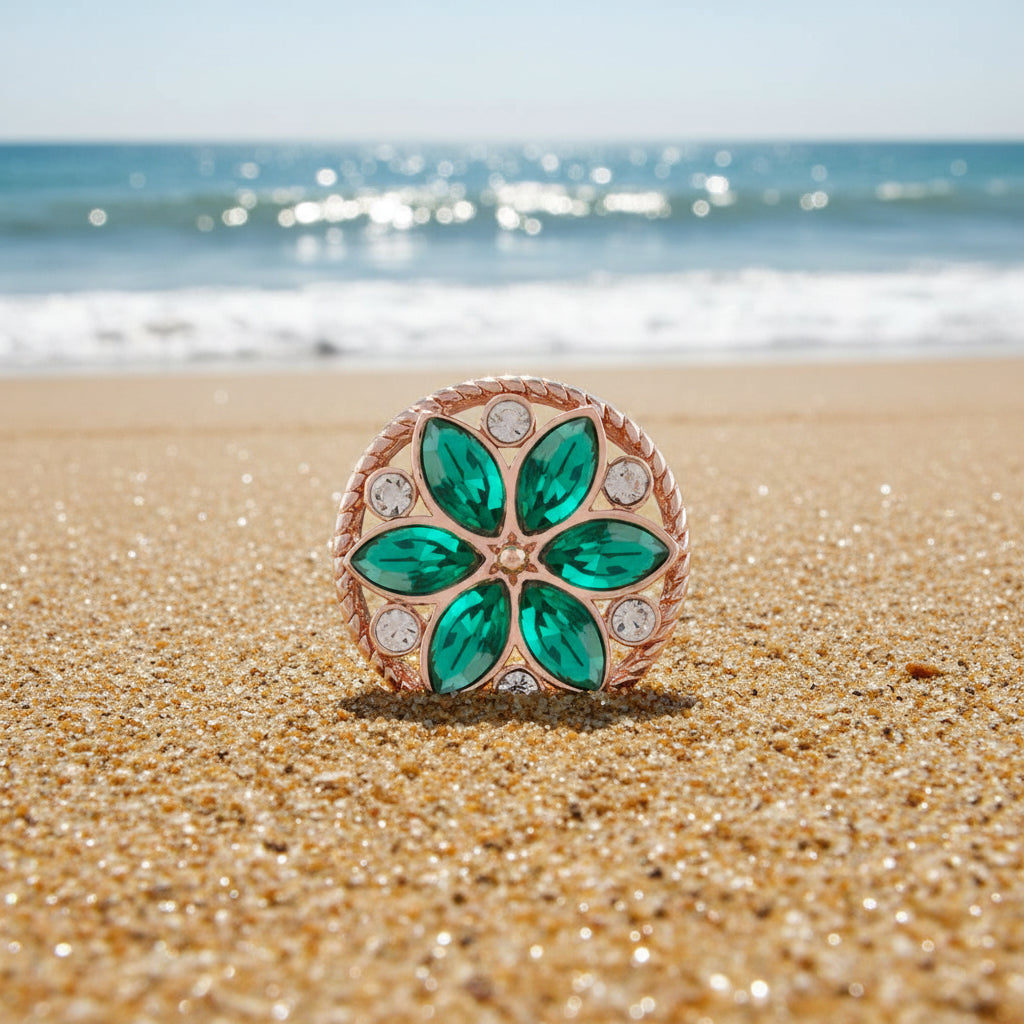 A circular floral snap button featuring six green marquise-cut crystals arranged in a flower pattern, surrounded by a rose gold rope-textured border and small clear round crystals