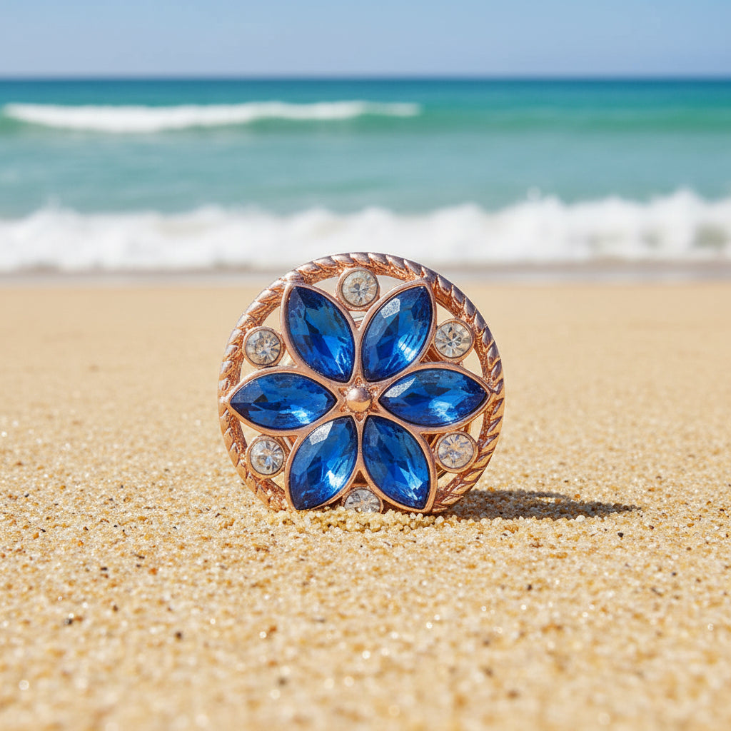 A round rose gold snap button featuring a floral design with five blue marquise-cut rhinestones in the center and four small clear round rhinestones around the border