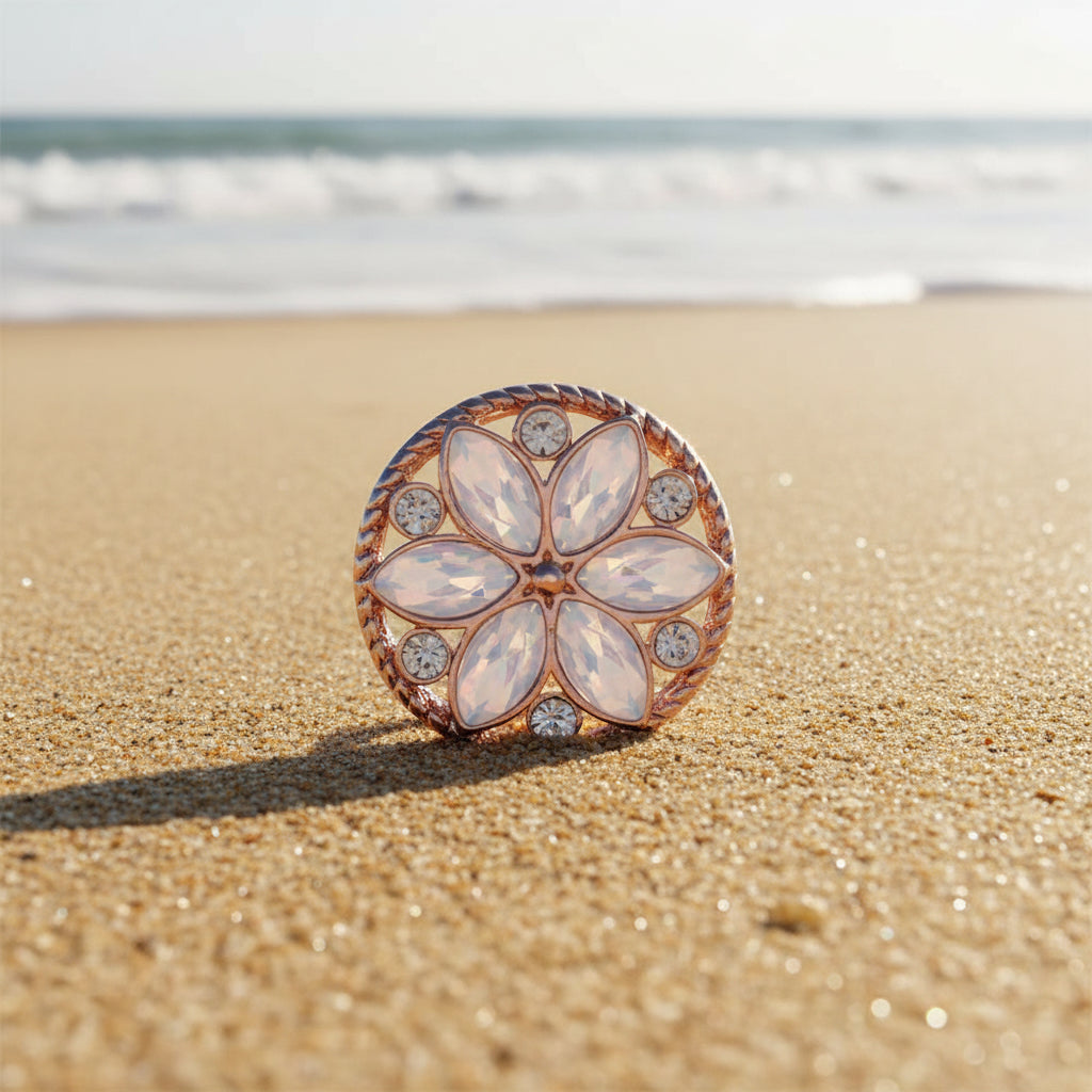 A round rose gold flower-shaped snap button with white marquise-cut stones and small clear rhinestones, set against a sparkly white glitter background.