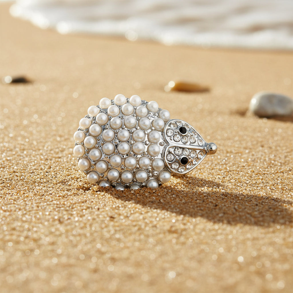 A silver-toned hedgehog snap button embellished with white faux pearls on its back and small clear rhinestones on its head, featuring black rhinestone eyes, set against a sparkly white background.