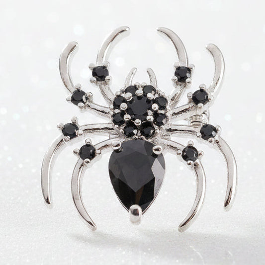A silver spider snap button with black gemstones, featuring a faceted black teardrop-shaped center stone and small black stones on its legs, set against a sparkly white background.