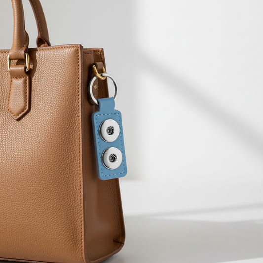 A light blue leather keychain featuring two circular silver-tone snap buttons and a silver split key ring.