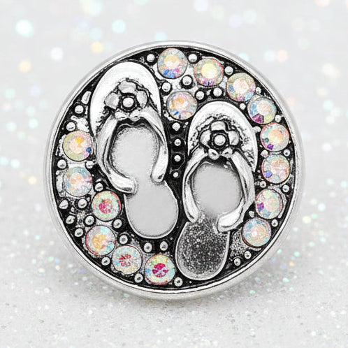 A circular silver-toned snap button featuring a pair of flip-flops surrounded by a border of iridescent rhinestones on a black background.