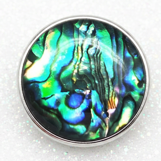 A circular snap button featuring an iridescent abalone shell pattern with vibrant blue, green, and teal colors, framed by a white border on a white background.