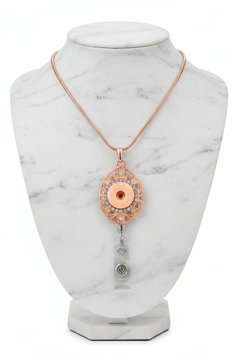 A rose gold oval pendant necklace with a filigree frame, a central rose gold disc, and a silver-and-clear retractable badge reel attachment below, shown on a white background.  A Snappy Jewels exclusive.