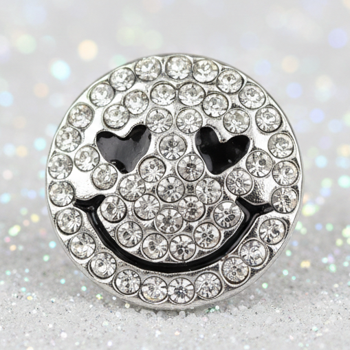A round silver-tone smiley face snap button embellished with clear rhinestones, featuring black heart-shaped eyes and a black curved smile.