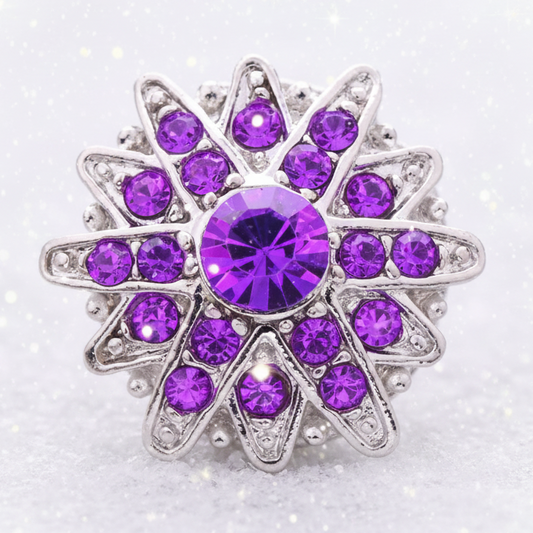 A silver-tone starburst ring featuring a large round purple crystal in the center, surrounded by multiple smaller purple and clear rhinestones on a white background.