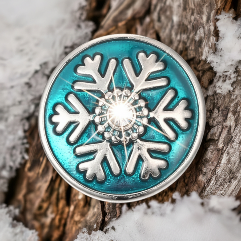 A round turquoise and silver snowflake charm with a clear crystal in the center, resting on a textured piece of wood with snow around it.