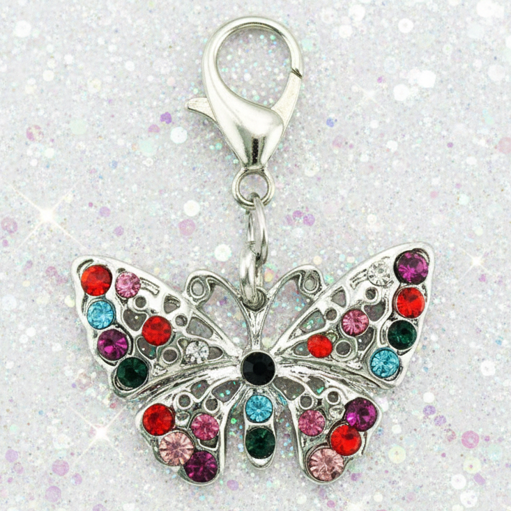 A silver butterfly-shaped charm embellished with colorful rhinestones in red, pink, blue, green, and black, attached to a silver lobster clasp, set against a sparkly white background.