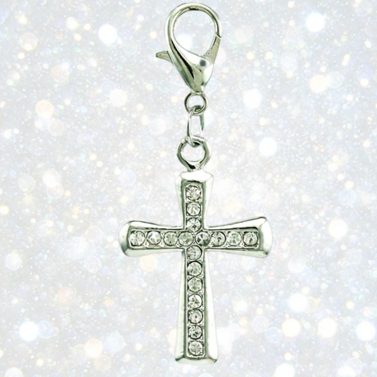 A silver cross charm embellished with clear rhinestones, featuring a lobster clasp at the top, set against a sparkling white background.