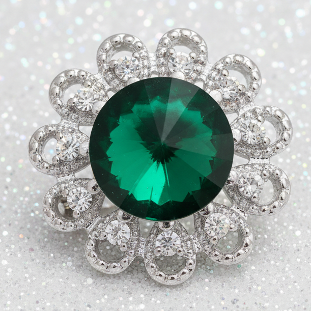 A silver-toned floral cluster snap button featuring a large round faceted green emerald-cut center stone surrounded by a halo of smaller clear stones in an openwork silver setting, shown on a plain white background.