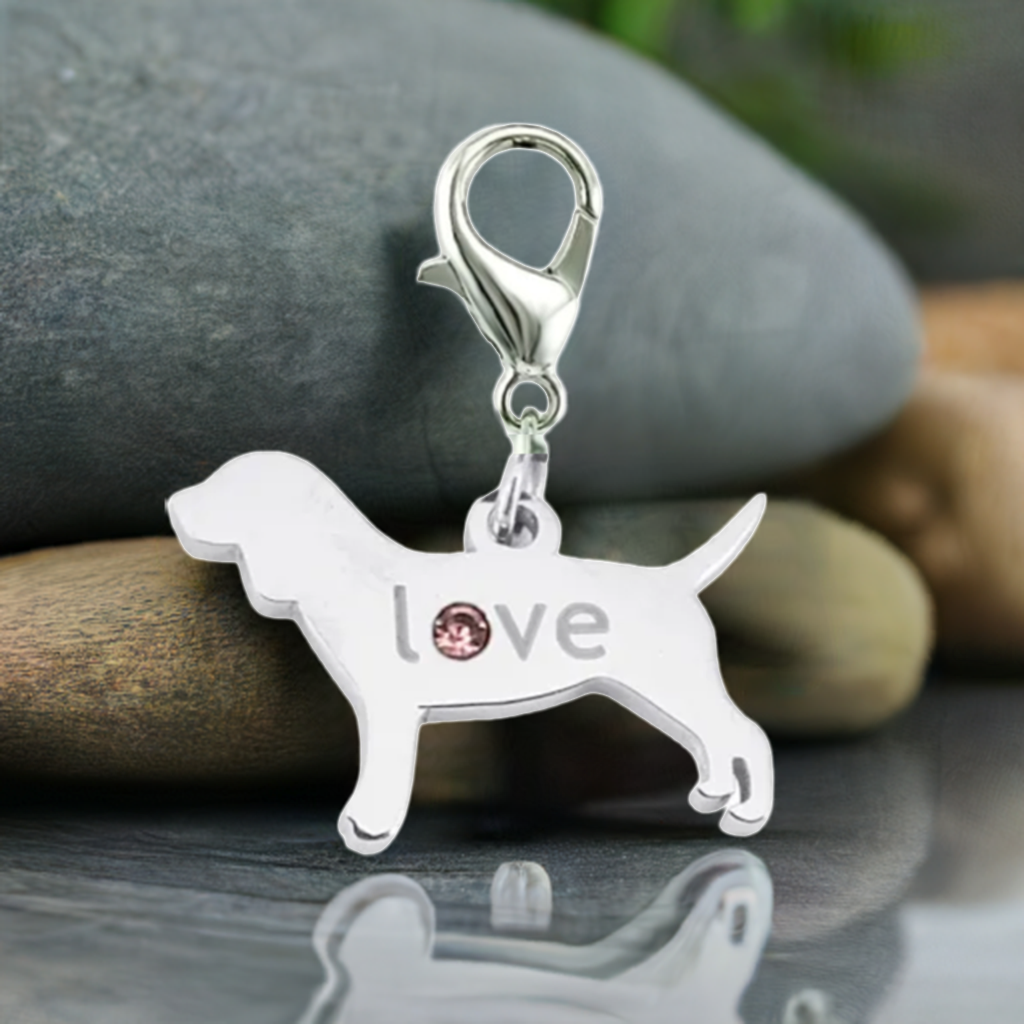 A silver dog-shaped charm pendant with the word 'love' and a small pink rhinestone, resting on stacked natural stones.