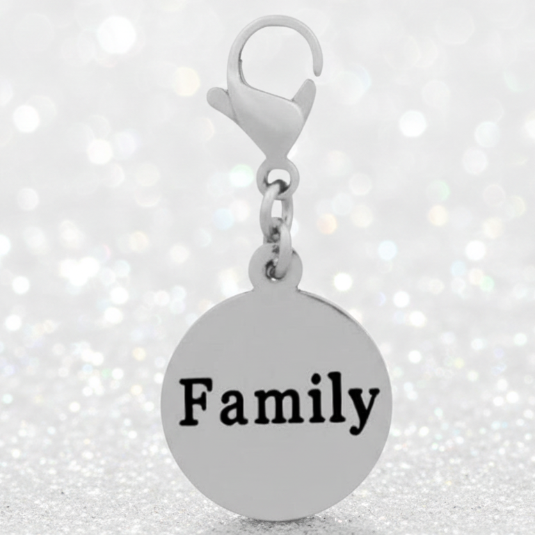 A silver round charm pendant engraved with the word 'Family' in black, attached to a silver lobster clasp, set against a sparkling white bokeh background.