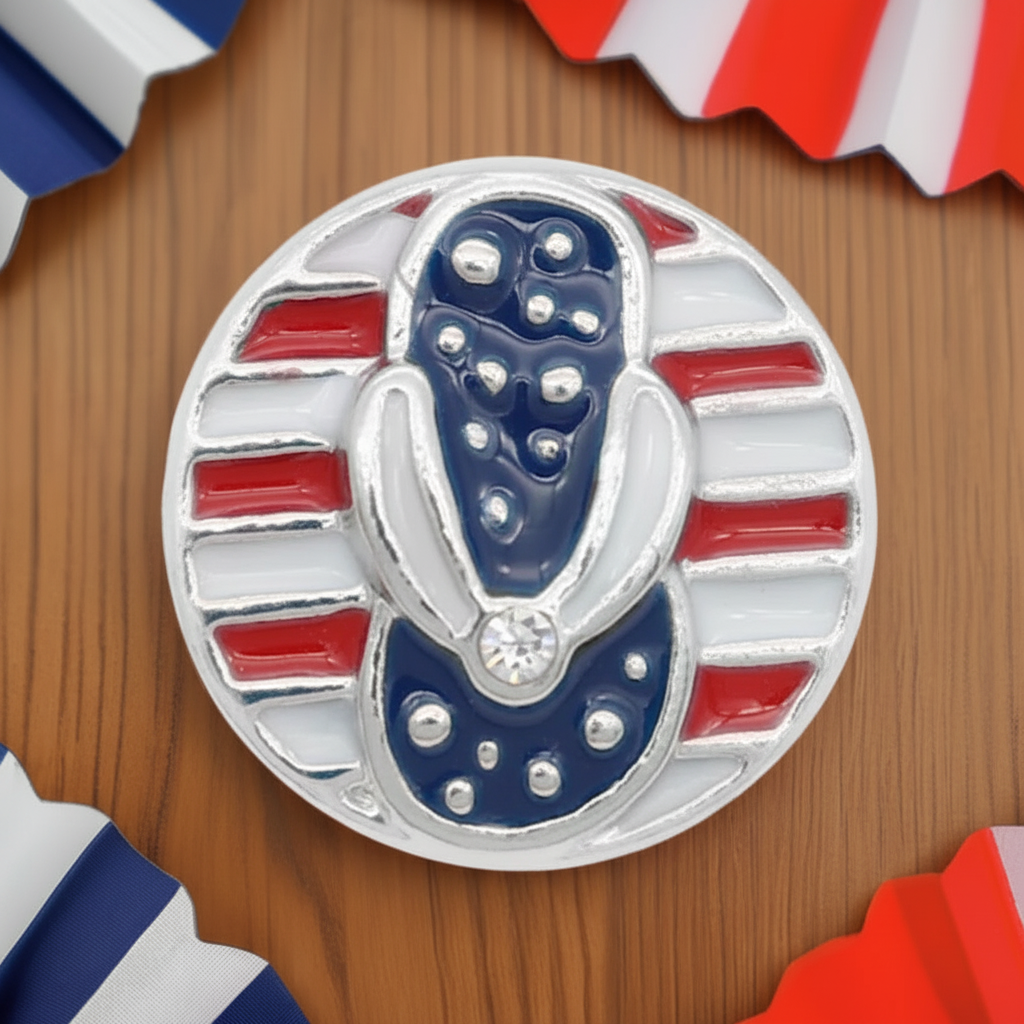 A circular silver-toned enamel snap button featuring a stylized helmet design in navy blue and white, surrounded by red and white stripes, displayed on a wooden surface with patriotic paper decorations in the corners.