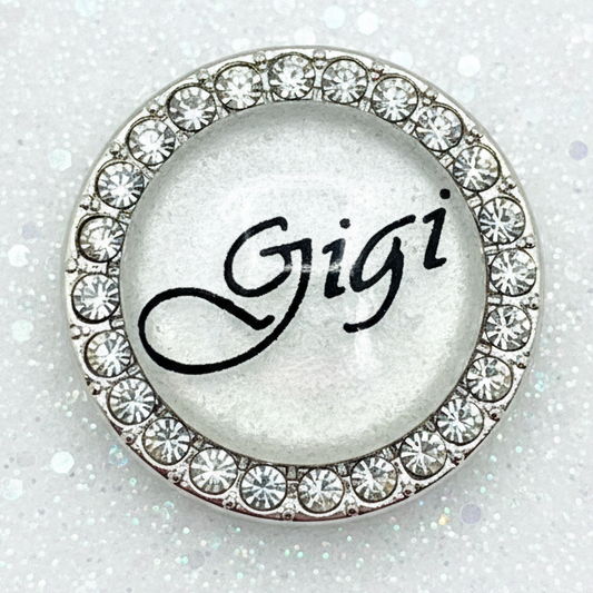 A round silver-toned snap with a border of clear rhinestones and the name 'Gigi' written in black script in the center.