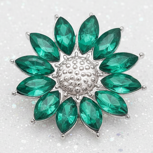 A flower-shaped snap featuring faceted green marquise-cut stones arranged in a circular pattern around a textured silver-toned center, set against a plain white background.