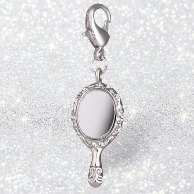 A silver charm shaped like a hand mirror with an ornate filigree frame and a lobster clasp, shown on a sparkling white background.