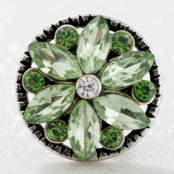A round floral snap button featuring faceted light green marquise and oval crystals arranged in a flower pattern, with smaller green round crystals around a central clear crystal, set in a dark silver-tone metal.