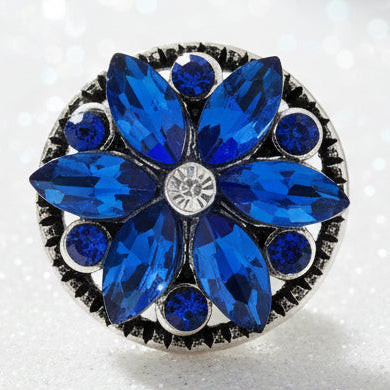 A round floral snap button featuring large blue marquise-cut and round crystals arranged in a flower pattern, with a clear crystal at the center and a silver-tone metal border.