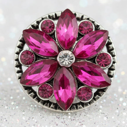 A silver-toned flower-shaped snap button featuring vibrant pink marquise and round crystals, with a small clear center stone, set against a sparkling white background.