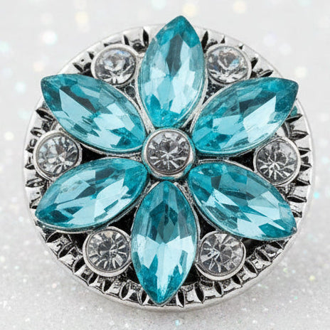 A round silver-tone snap button featuring a floral design with faceted light blue marquise-cut stones and smaller clear rhinestone accents, shown on a plain white background.
