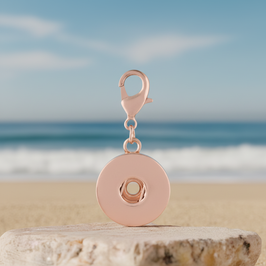 A rose gold magnetic snap button clasp with a lobster clasp, displayed on a stone surface with a blurred blue sky and sea background.