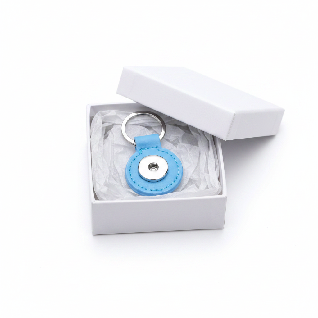 A light blue leather keychain with a silver metal key ring and snap button, presented inside an open white gift box with tissue paper.